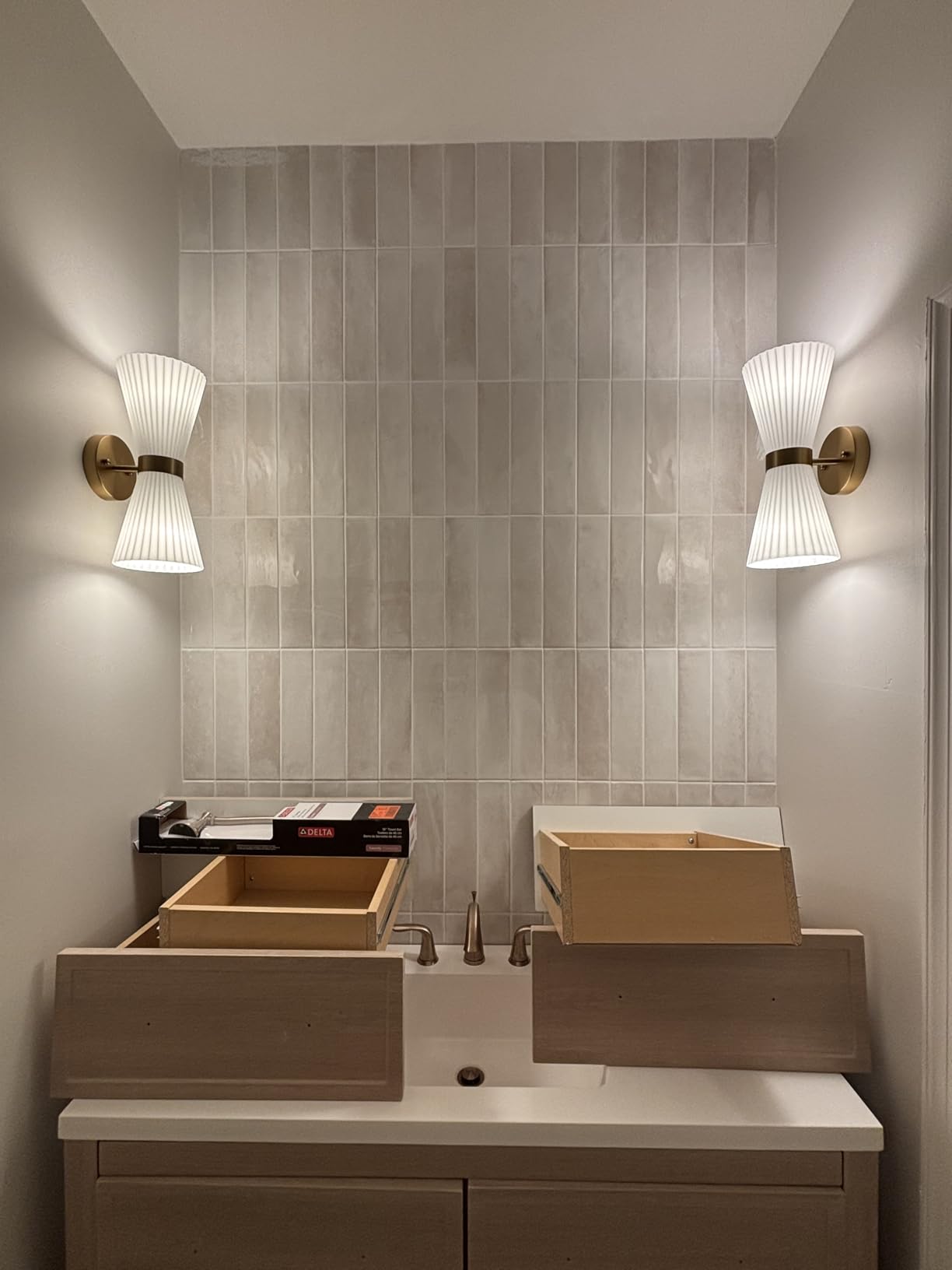 Bathroom vanity with dual sinks and wall lights on a tiled wall.