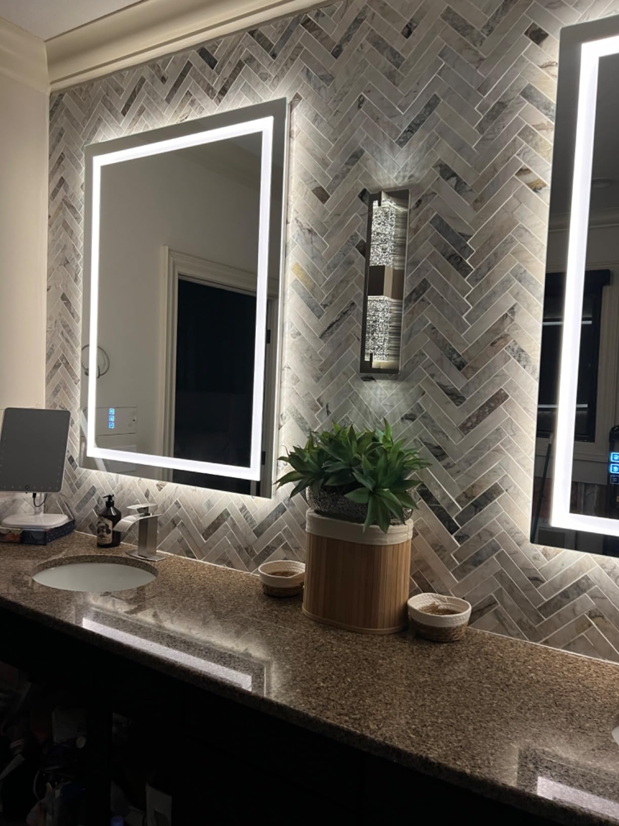 Bathroom vanity with illuminated mirror, plant, and decorative wall tiles.