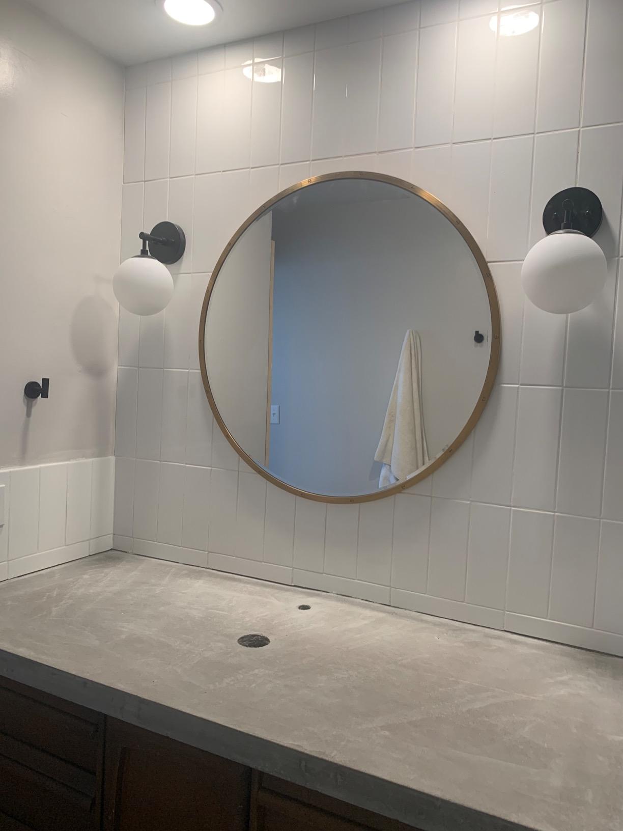 Bathroom with round mirror, tiled walls, and a countertop.