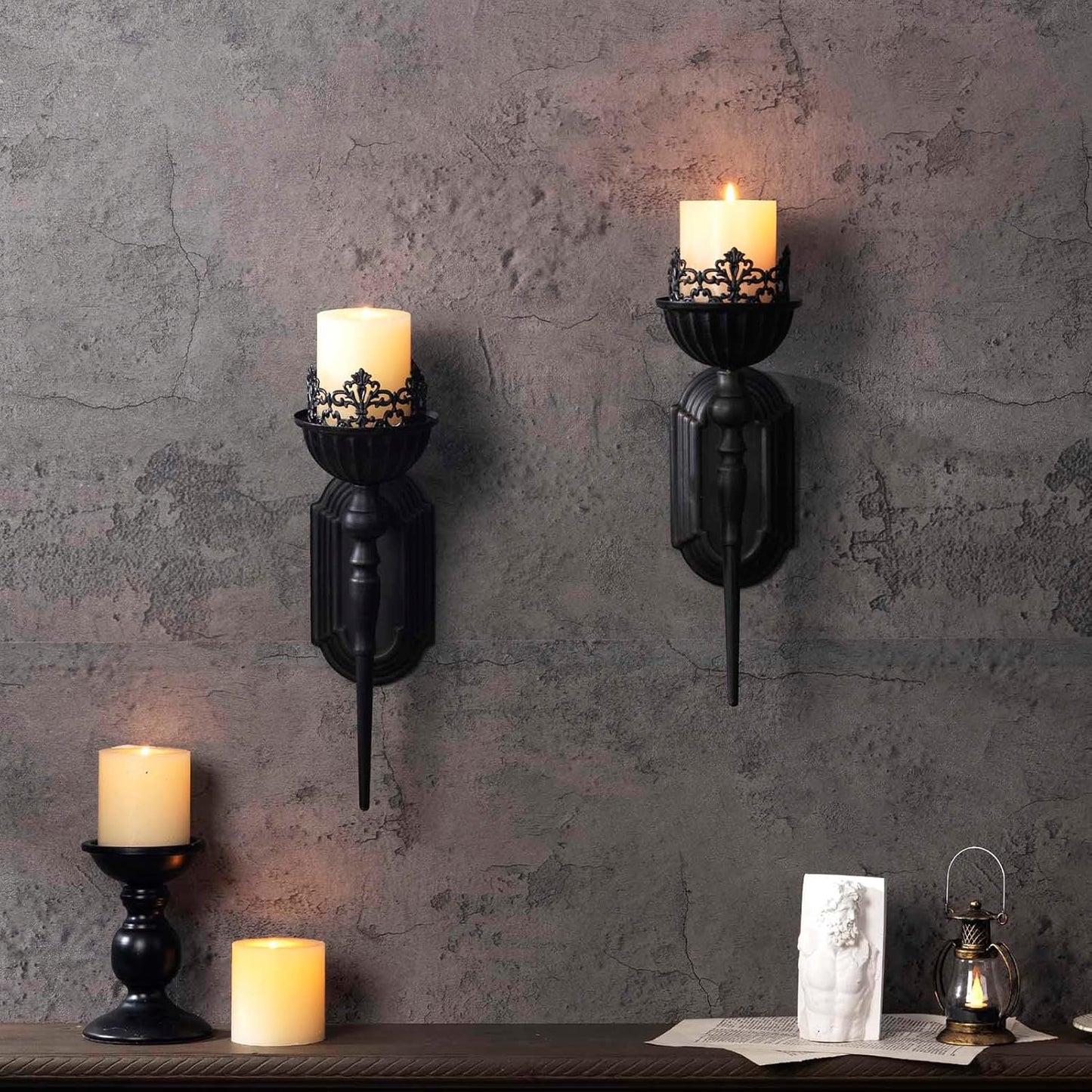 Black wall sconces with candles on a textured gray wall.
