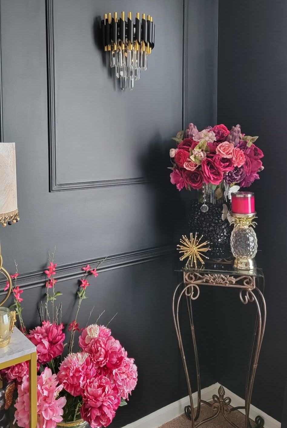 Decorative interior setting with flowers, candles, and a wall sconce on a dark wall.