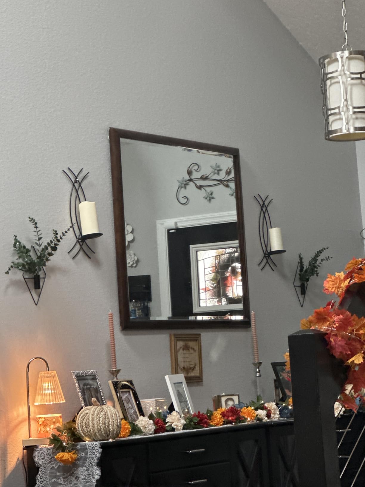 Decorative setup with a mirror, candles, and autumn-themed decor on a table against a gray wall.