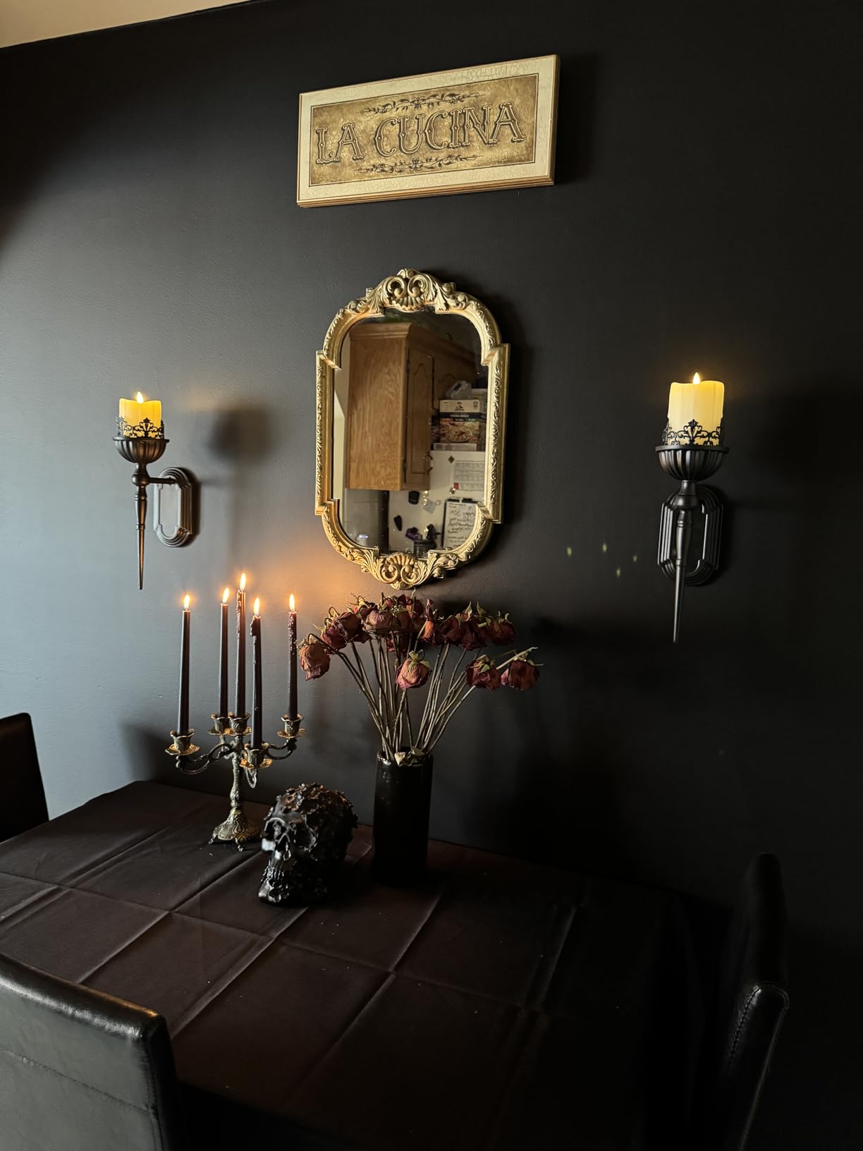 Decorative setup with candles, mirror, and skull on a dark wall.