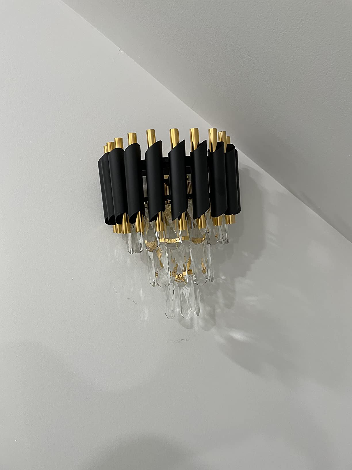 Decorative wall light fixture with black, gold, and clear accents on a white wall.