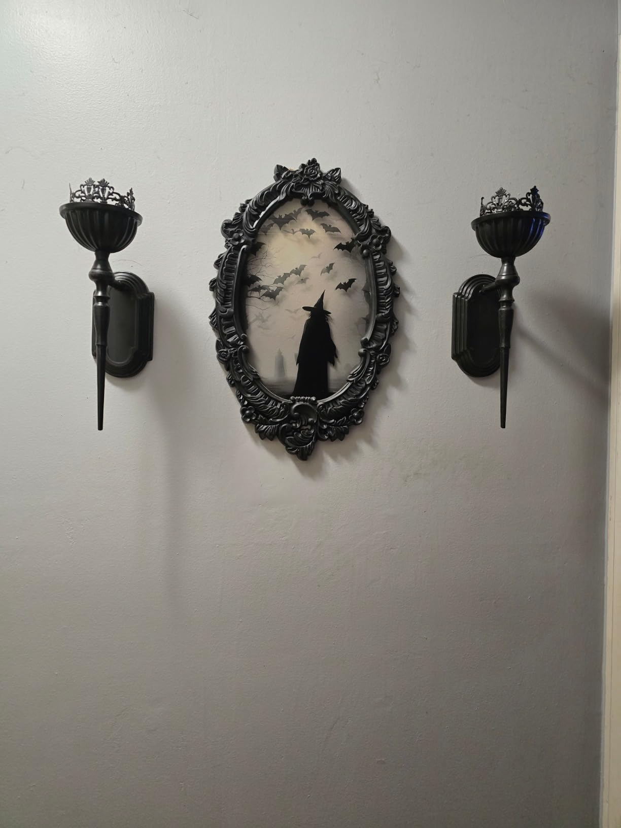 Decorative wall piece with black frame and candle sconces on a white wall