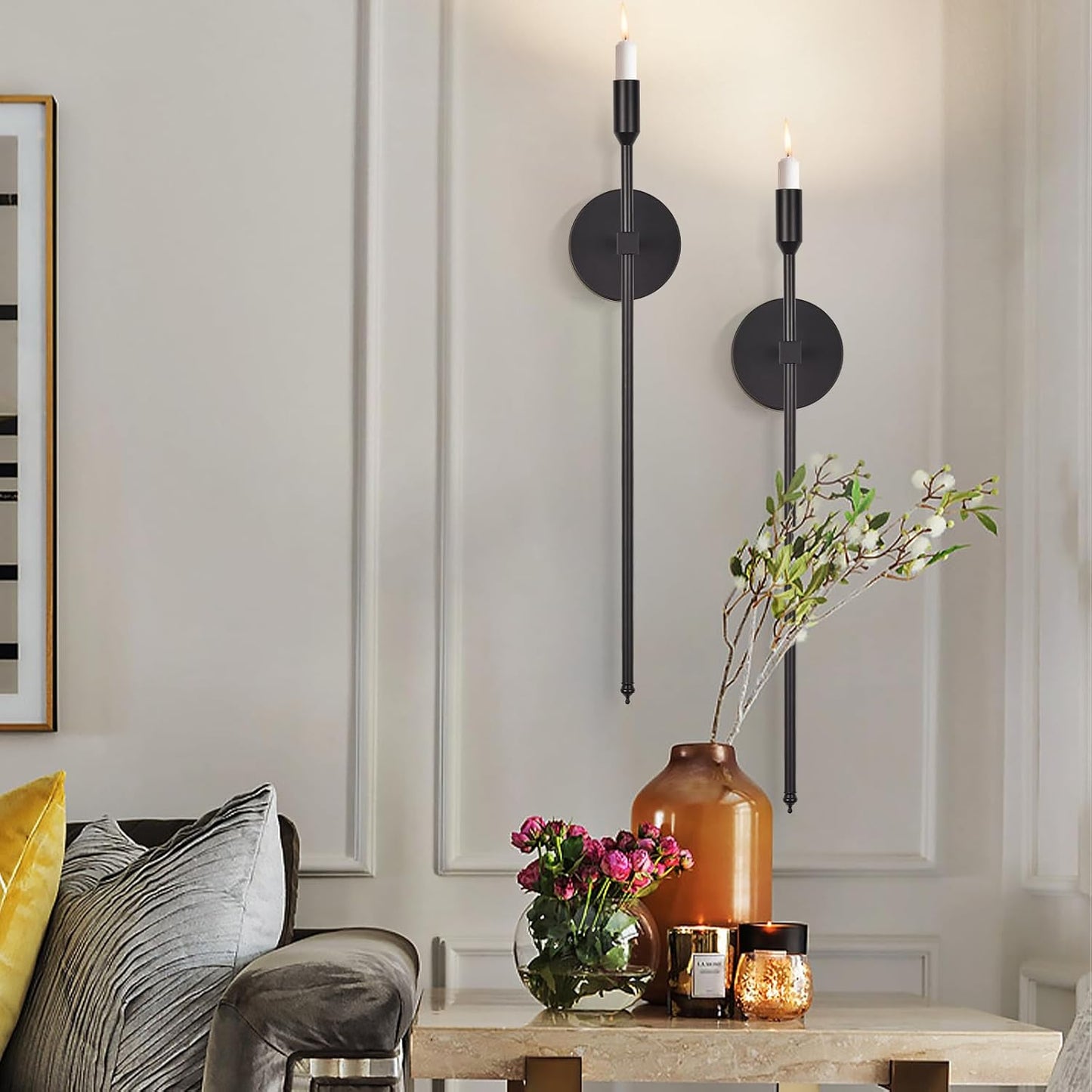 Decorative wall sconces with a vase of flowers and candles on a table in a room.