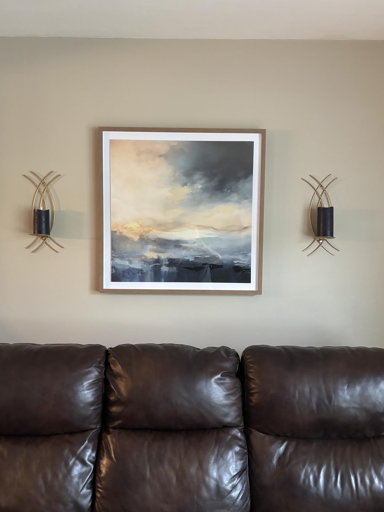 Framed artwork on a wall above a brown leather sofa with wall sconces.