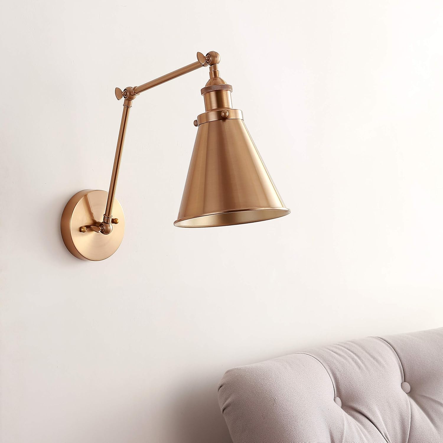 Gold wall lamp with adjustable arm on a light beige wall.
