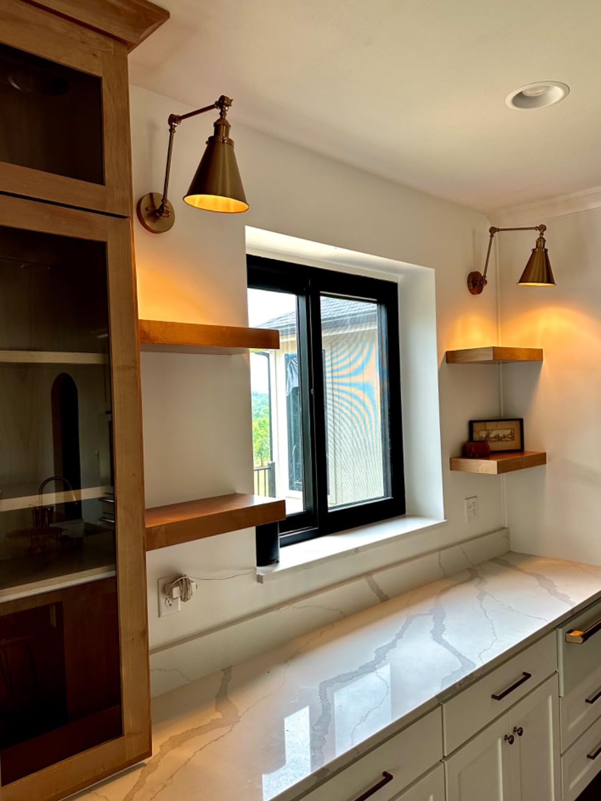 Modern kitchen with marble countertop, wooden shelves, and wall lights.