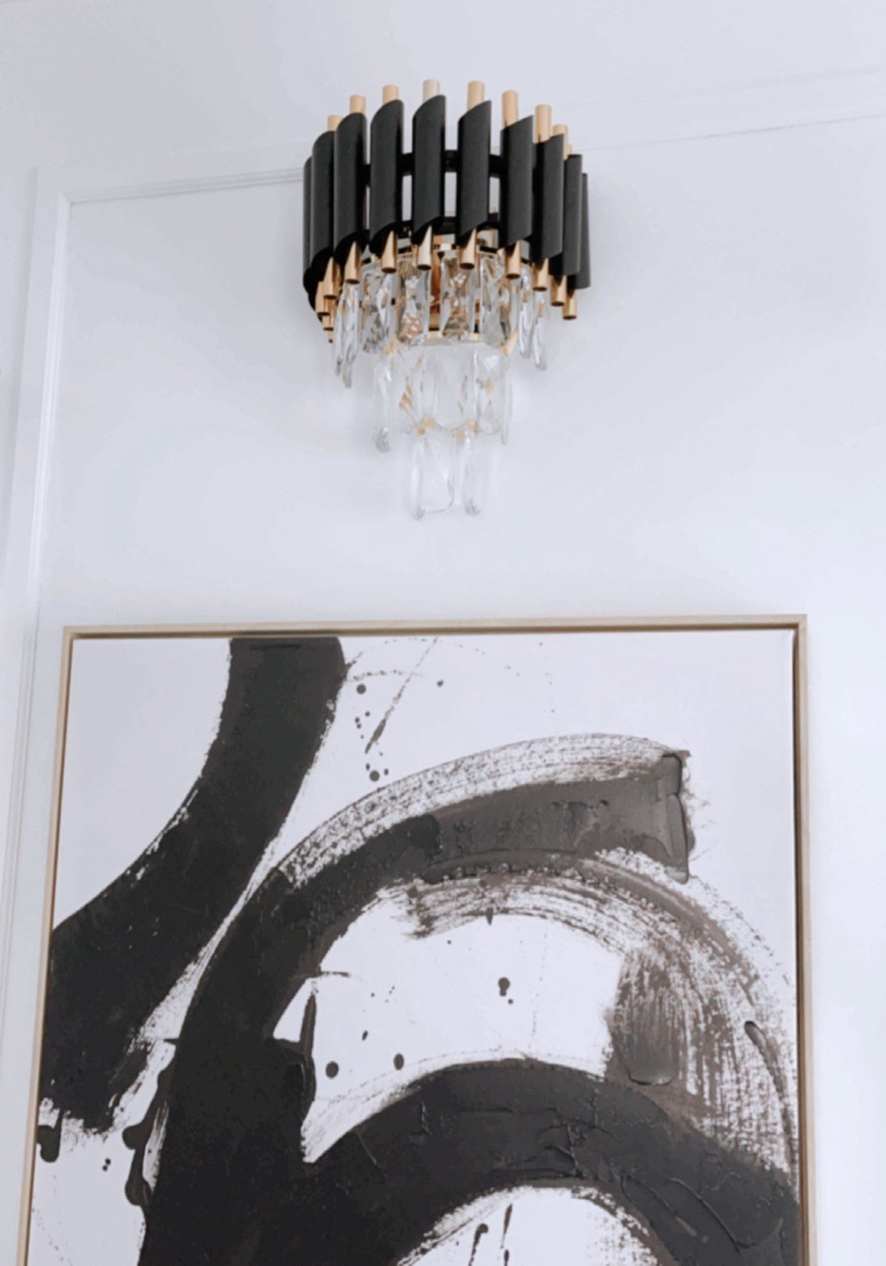 Modern wall light fixture with black and gold design above abstract art on a white wall.