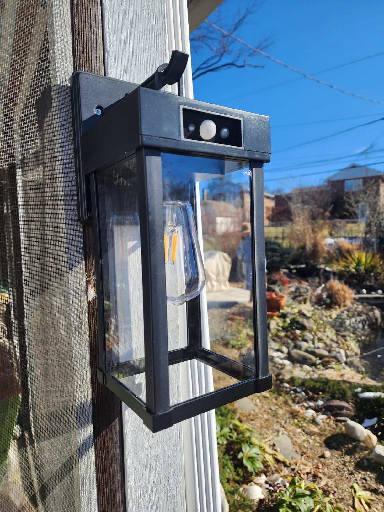 Solar light attached to a wooden post with a garden and blue sky in the background in  a day light