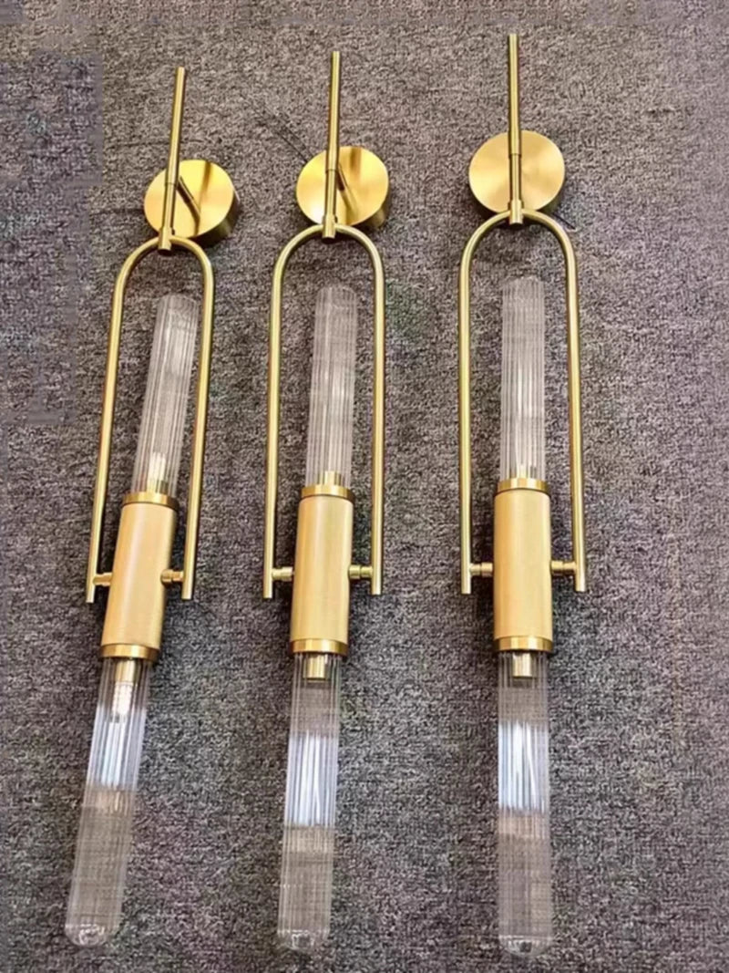 Three gold wall sconces with clear glass shades on a textured gray background