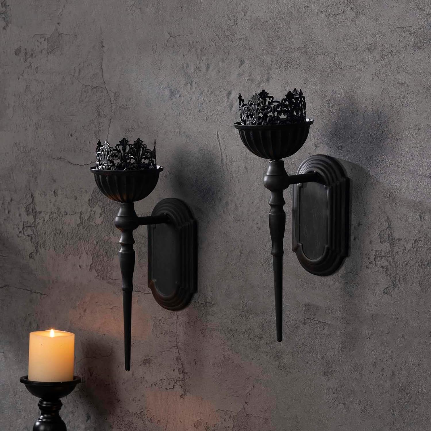 Two black wall sconces with decorative candle holders on a textured gray wall.