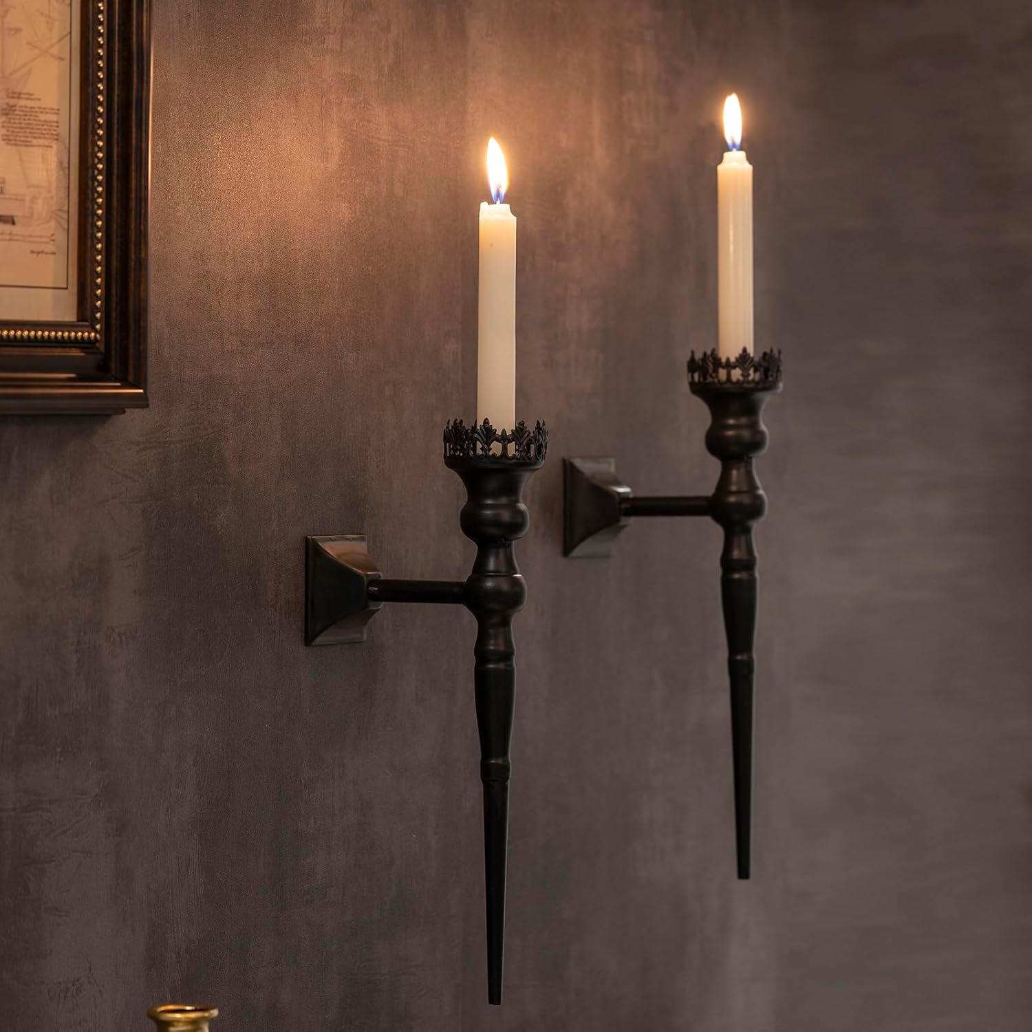 Two black wall sconces with lit candles on a textured wall.
