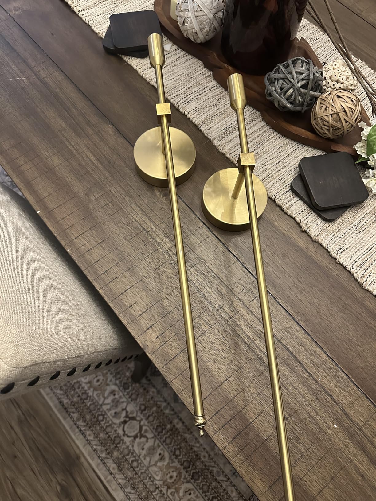 Two gold candle holders on a wooden surface with decorative items in the background.