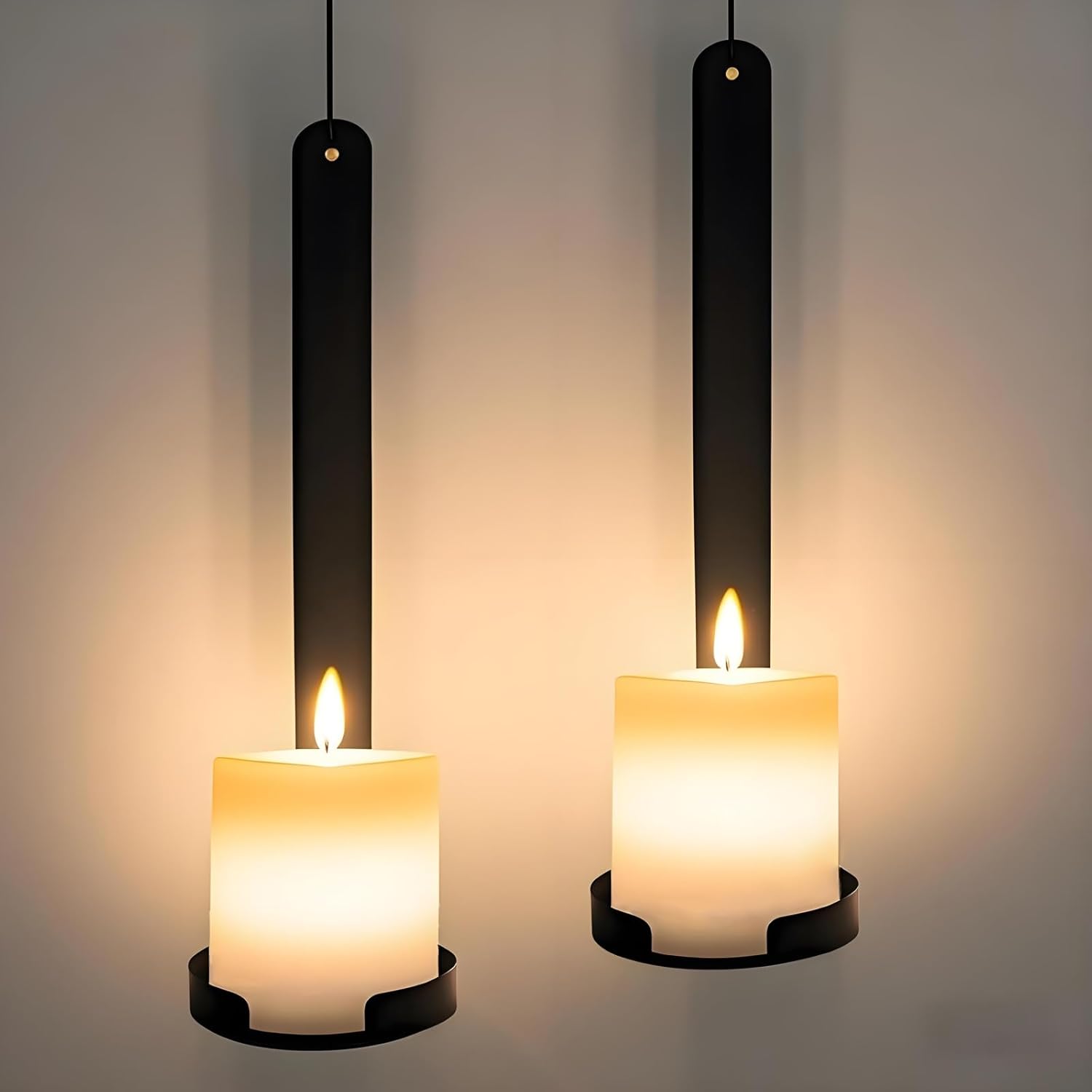 Two hanging candles with black holders on a neutral background