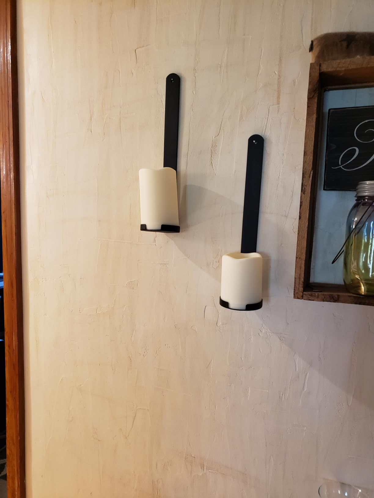 Two wall-mounted candle holders with candles on a light-colored wall.