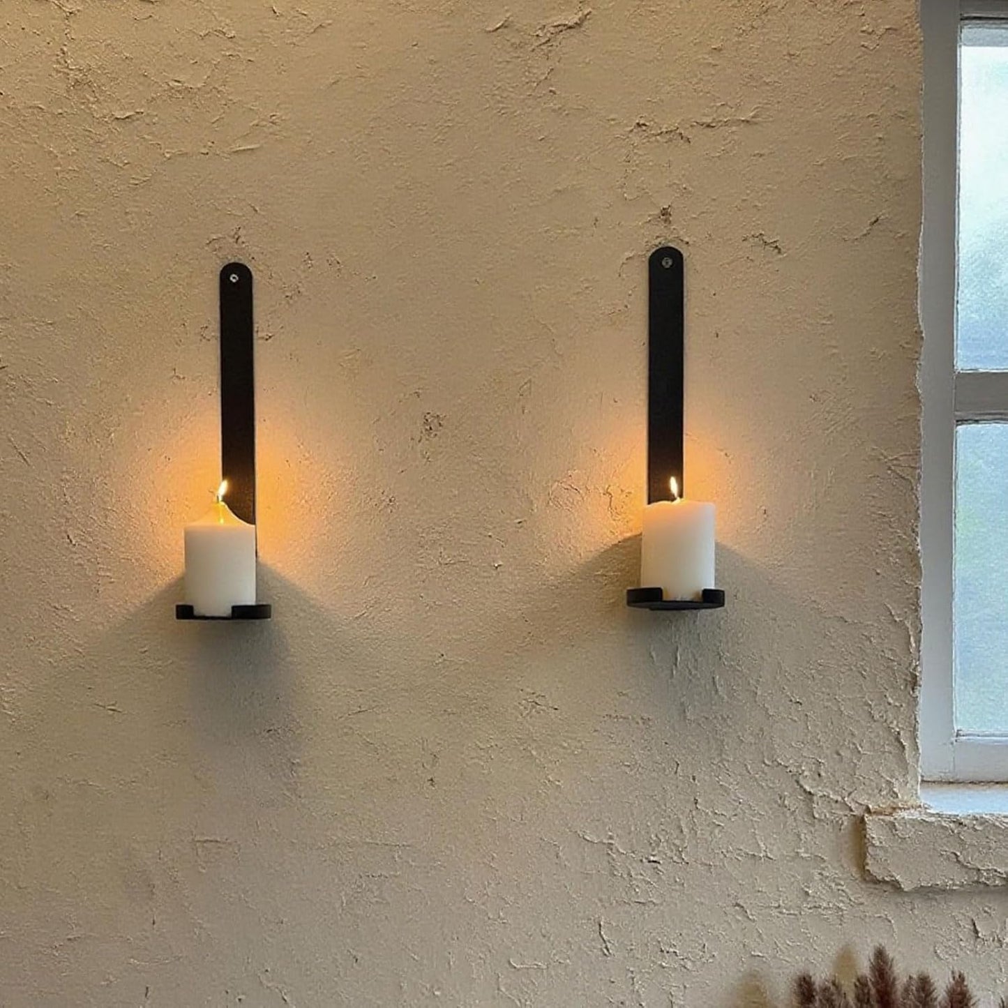 Two wall-mounted candle holders with candles on a textured wall.