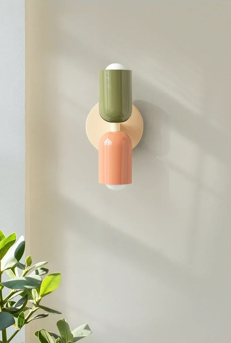 Wall-mounted lamp with green and pink design on a light gray wall.