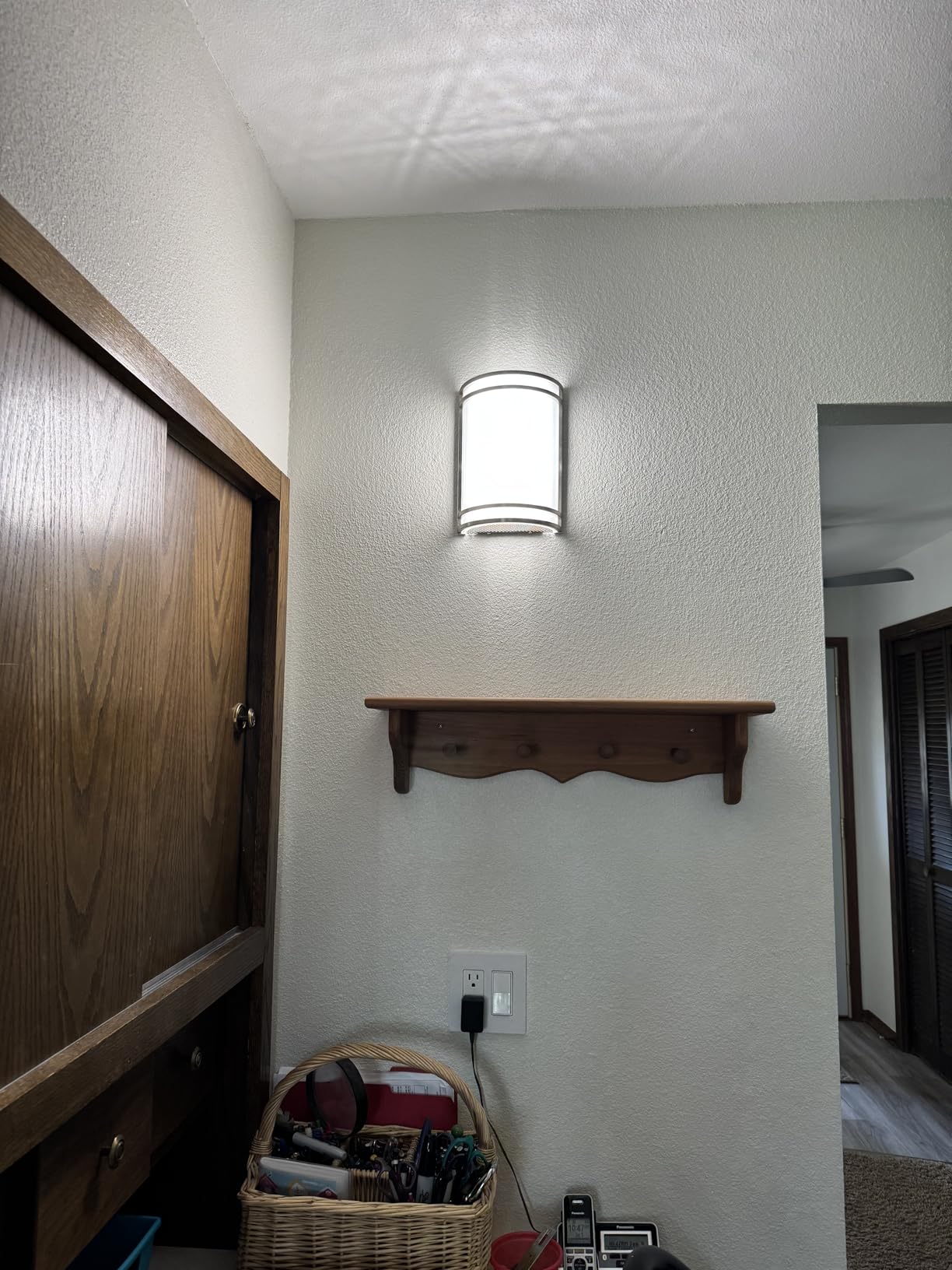 Wall-mounted light fixture above a wooden shelf in a room with a textured wall.
