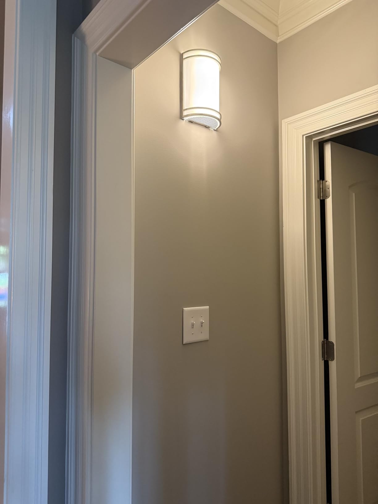 Wall-mounted light fixture on a gray wall with a door partially visible.