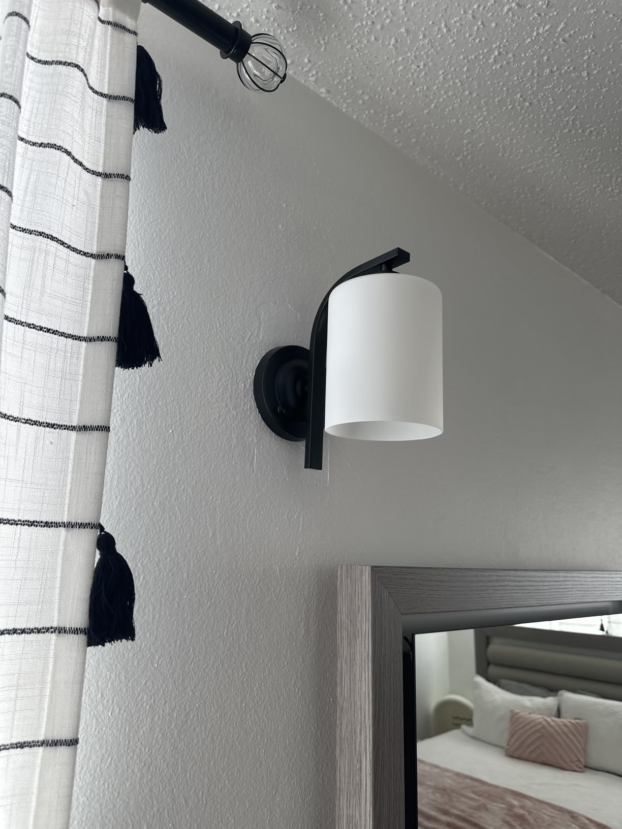 Wall-mounted light fixture with a white shade and black fixture against a neutral wall.
