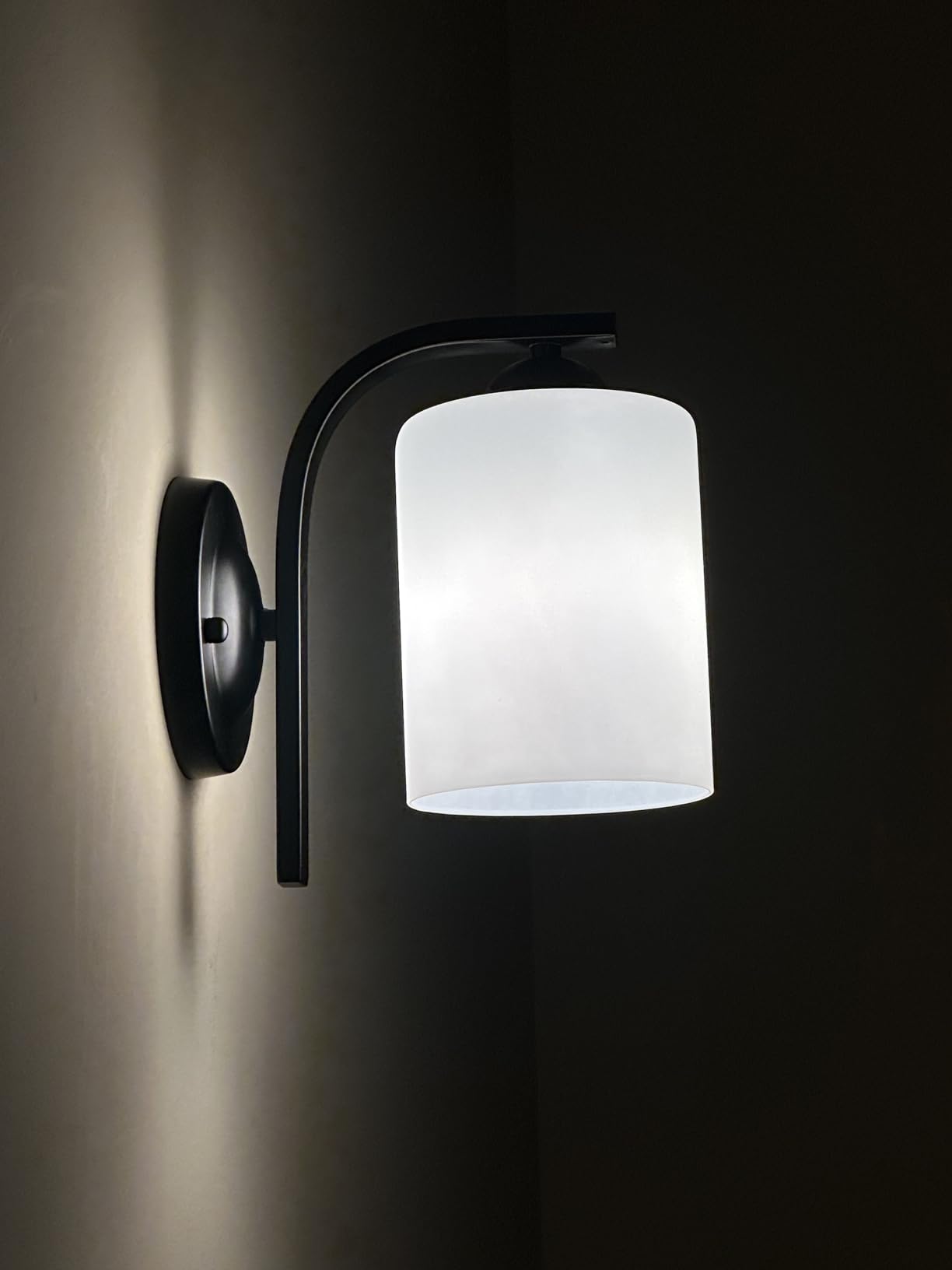 Wall-mounted light fixture with white glass shade on a dark background