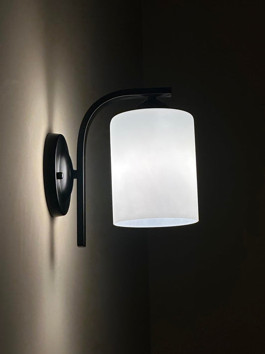 Wall-mounted light fixture with white glass shade on a dark background