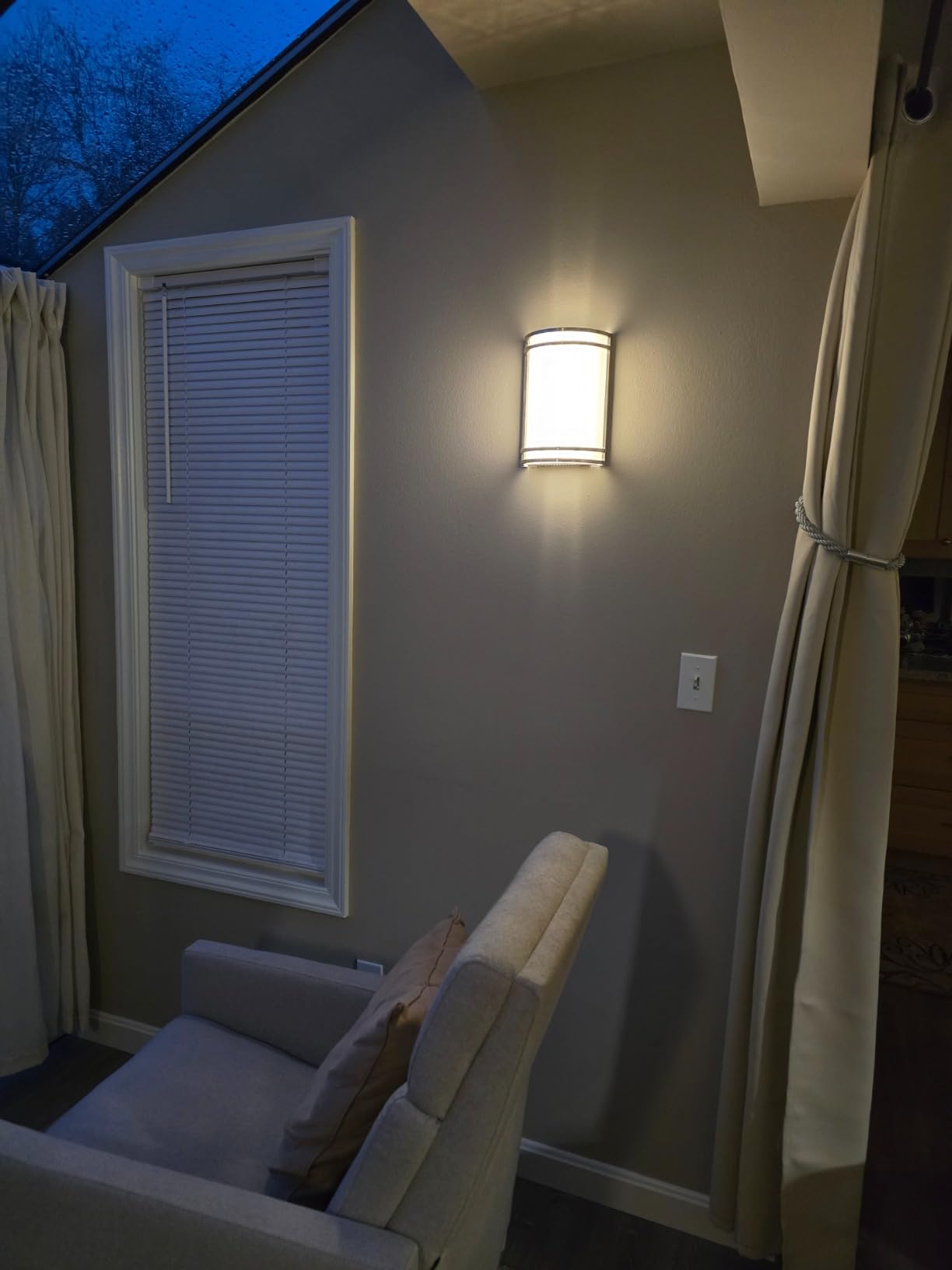 Wall sconce light fixture on a wall next to a window with blinds in a room.