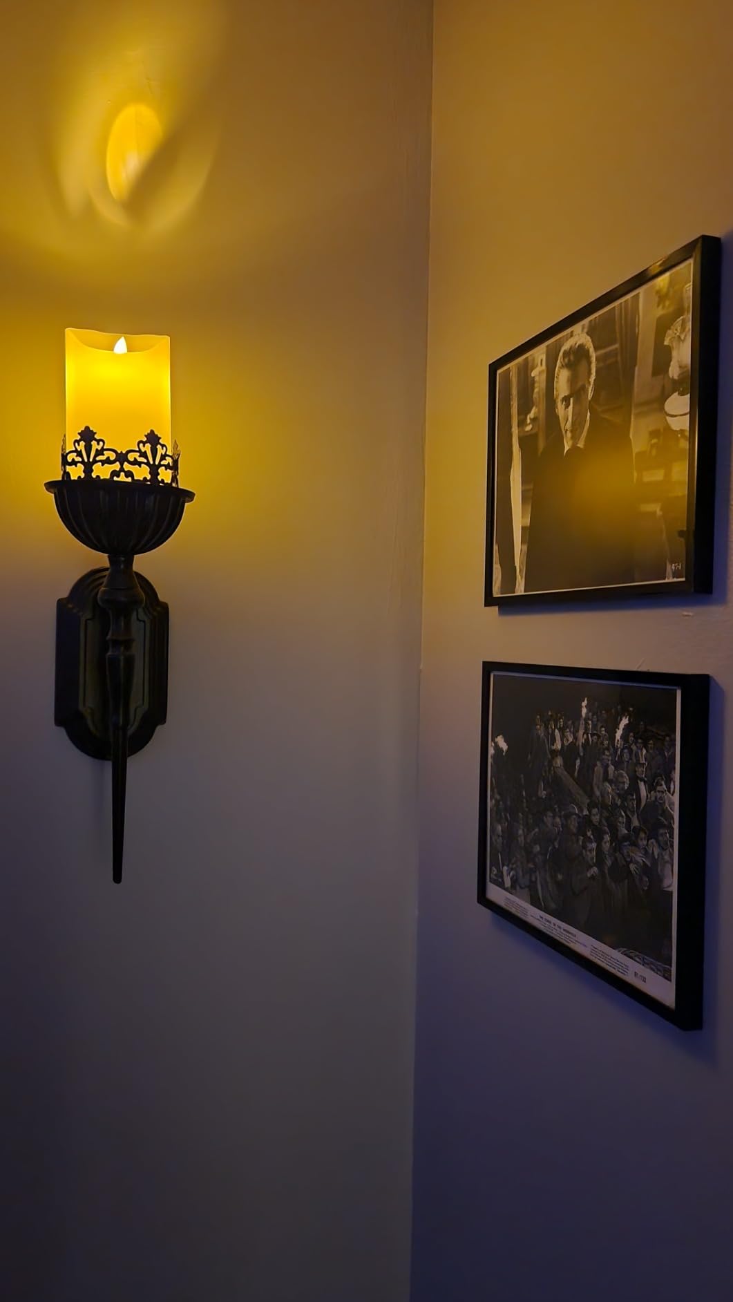Wall sconce with a candle on a wall with framed pictures.