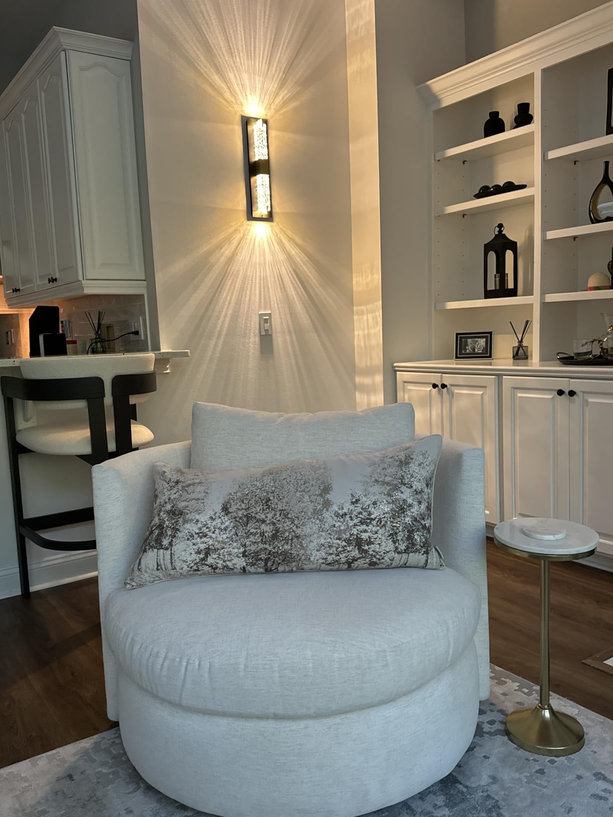 White armchair with a decorative pillow in a room with a wall sconce and shelves.