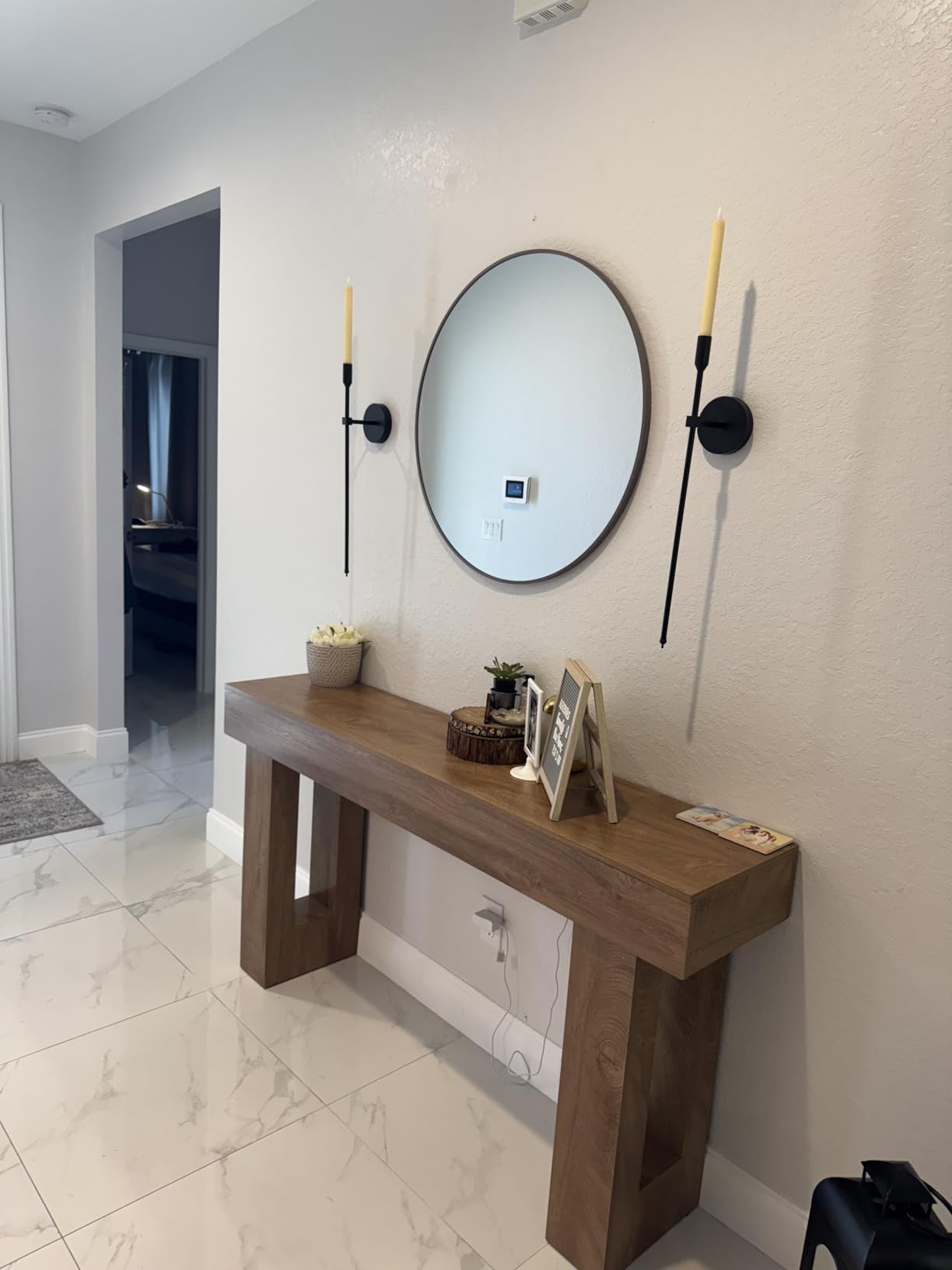 Wooden console table with decorative items against a wall with a round mirror and sconces.